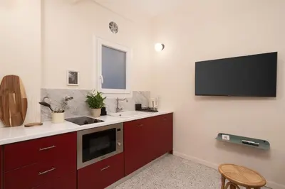 a kitchen with red cabinets and a tv on the wall at Cozy 1BR Apt near Acropolis & Metro In Koukaki in Athens
