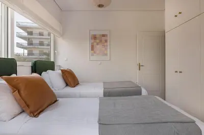 two beds in a room with white walls and a window at The Glyfada Getaway 3BR with Balcony by UPSTREET in Athens