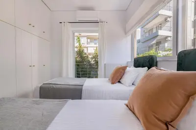 two beds in a white room with a window at The Glyfada Getaway 3BR with Balcony by UPSTREET in Athens