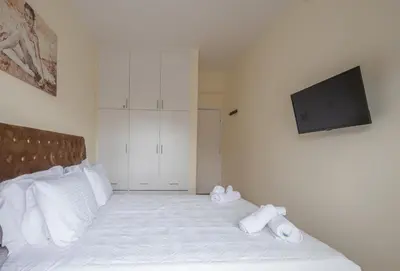 a white bed with white pillows and a flat screen tv at ANDIE Kallithea Apartment in Athens