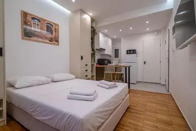 a white bedroom with a bed and a kitchen at The Honeycomb Suite in Athens