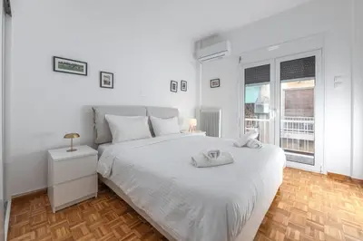 a white bedroom with a large white bed and two windows at Colorful Koukaki Apartment Near the Acropolis in Athens