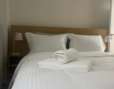 a stack of towels on a white bed with pillows at Κομψό Διαμέρισμα στο Πασαλιμάνι in Piraeus
