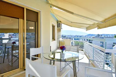 a balcony with a glass table and white chairs at Cosy modern flat under the Acropolis in Athens