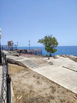 a sidewalk next to the ocean with a tree at By the wave luxurious studios in Piraeus