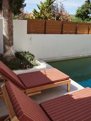 a wooden bench next to a swimming pool at Camara Athens Riviera Home in Aghia Marina