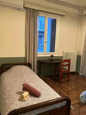 a bedroom with a bed and a table and a window at Private room for 3 in a dorm 5' from metro in Athens