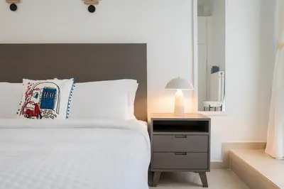 a bedroom with a white bed and a night stand with a lamp at Thalè Residence Varkiza in Vari