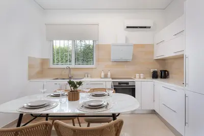 a white kitchen with a white table and chairs at Thalè Residence Varkiza in Vari