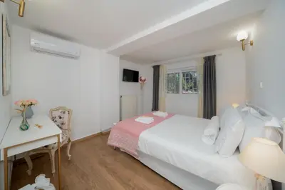 a white bedroom with a bed and a desk and a window at Livingstone House in Porto Rafti