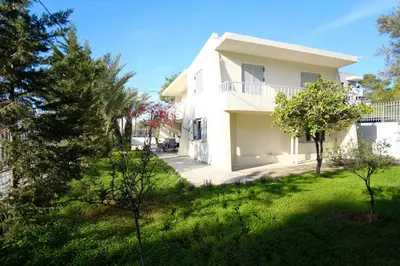 a white house with a green yard and trees at Apartment Theros near the beach in Anavissos