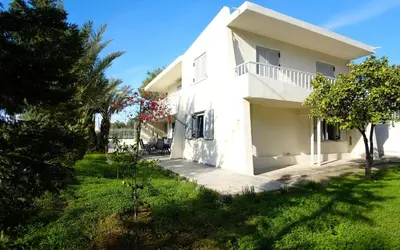 a white house with a green yard and trees at Apartment Theros near the beach in Anavissos