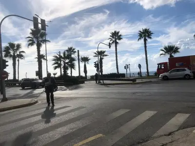 a person crossing a street in a crosswalk with palm trees at Sweet Apartment By The Sea in Athens
