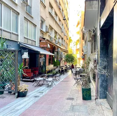 an empty street with tables and chairs and buildings at Athenian blue in Athens