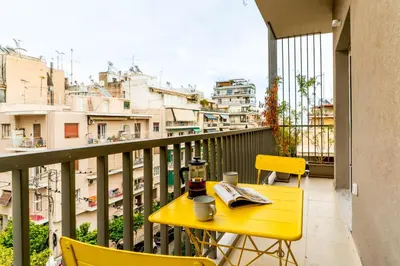 a yellow table and chairs on a balcony with buildings at Buena Vista by Pame Rentals in Piraeus