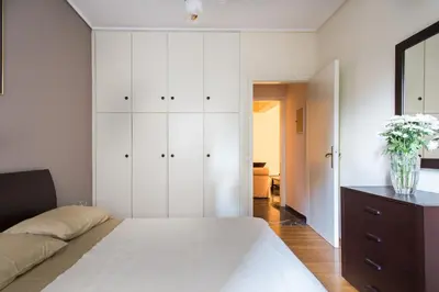 a white bedroom with a bed and a vase of flowers at A perfect place - close to Acropolis & Seacoast in Athens