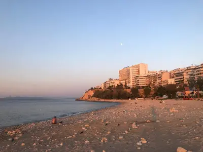 a beach with buildings and people sitting on the beach at Promenade Piraeus in Piraeus
