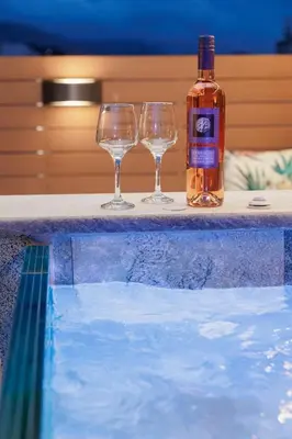 a bottle of whiskey and two wine glasses sitting next to a swimming pool at Elysium Heated Jacuzzi with Acropolis View in Athens