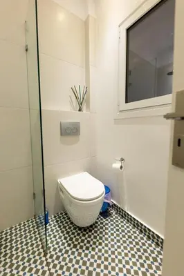 a bathroom with a toilet with a window and a tiled floor at HeKo Collection Athens 2 in Athens