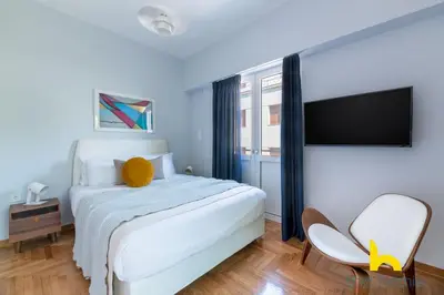 a bedroom with a white bed and a flat screen tv at Retro Radiance Artistic Haven Near Acropolis in Athens
