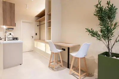 a kitchen with two white stools and a table and a plant at AVM Suites - Grand Thissio Prestige Residence in Athens