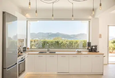 a kitchen with white cabinets and a large window at Athens Riviera Villa overlooking the Aegean sea in Anavissos