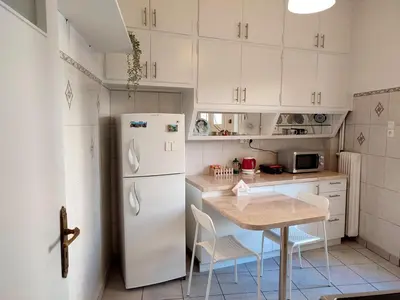 a white kitchen with a table and a refrigerator at Feels like home in Athens center in Athens