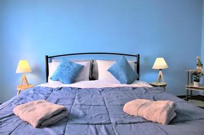 a bed with two pillows on it with a blue wall at Cosy executive room in beautiful n quiet flat in Athens