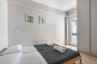 a white bedroom with a bed and a window at South Blue Beach & Park Apartment in Vouliagmeni in Athens
