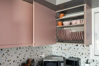 a kitchen with pink cabinets and plates on shelves at South Blue Beach & Park Apartment in Vouliagmeni in Athens