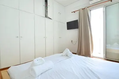a white bedroom with towels on a bed with a window at A cute and comfortable two bedroom apartment in Piraeus