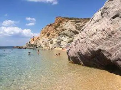 a beach with people in the water and a large rock at Thimari Sports & Spa with private pool and jacuzzi in Sounio
