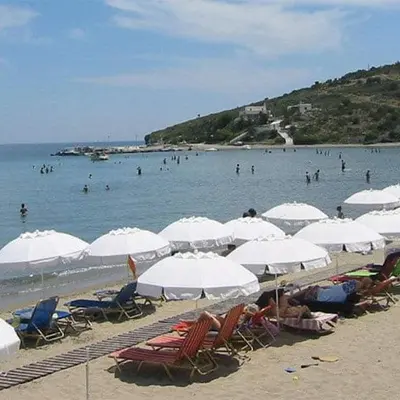 a beach with white umbrellas and people in the water at Svetlana & Michalis Oasis Hotel in Agia Marina Aegina