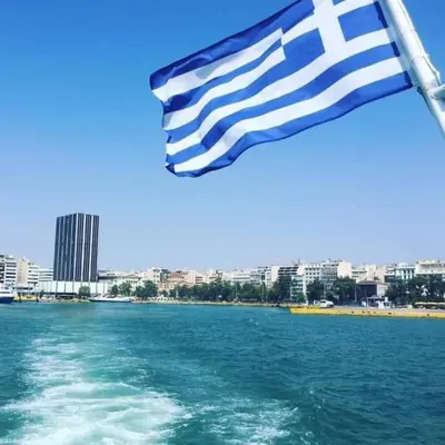 a flag flying over the water with a city in the background at Hotel Niki Piraeus in Piraeus