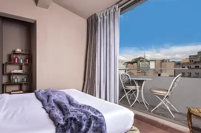 a bedroom with a bed and a balcony with a table at iFeel Athens in Athens