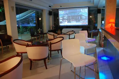 a restaurant with white chairs and a bar with a television at Galini Hotel in Agia Marina Aegina
