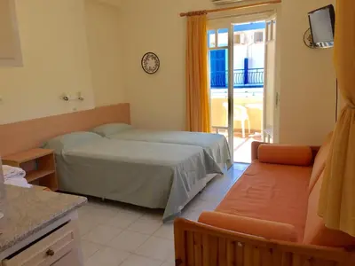 a bedroom with a bed and a couch and a balcony at Sylvia Studios in Agia Marina Aegina