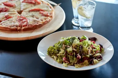 a table with a plate of salad and a pizza at Candia Hotel in Athens