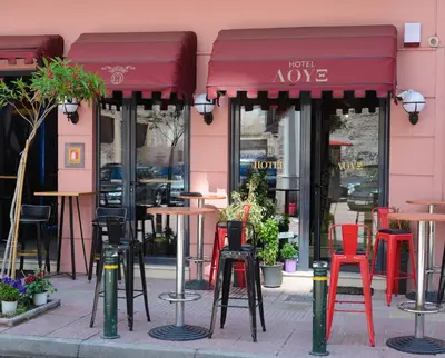 a row of tables and chairs in front of a pink building at LUX Hotel in Piraeus