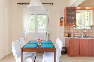 a dining room table with white chairs and a kitchen at Markella's House in Vravrona