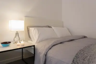 a bed with white pillows and a table with a lamp at Homz Studios Faliro in Athens