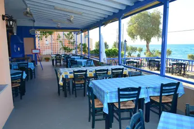 a restaurant with blue tables and chairs and the ocean at Aiolos in Vaia