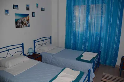 two beds in a bedroom with blue drapes at Cosy Apartment Pinotsi in Athens