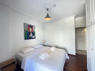 a bedroom with a white bed with a painting on the wall at Aries - Glyfada City Center Apartment in Athens