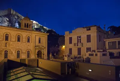 a group of buildings at night with a church at Tripodon Plaka In the shade of Acropolis by GHH in Athens
