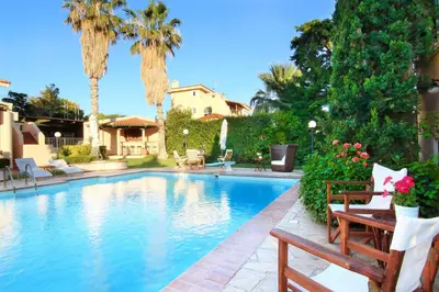 a swimming pool with two benches and palm trees at Oasis Pool House by GHH in Lagonissi