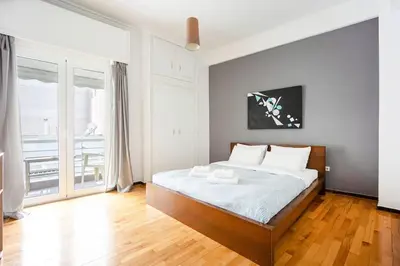 a bedroom with a bed with white sheets and wooden floors at Apartment in the Middle of Everything in Athens