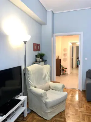 a living room with a white chair and a flat screen tv at Koukaki Apt 5 min walk to Acropolis in Athens