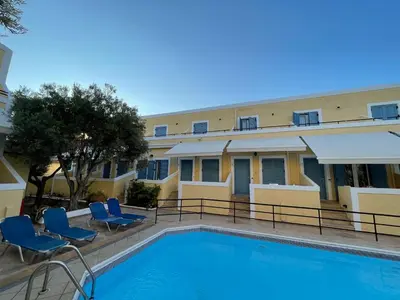 a swimming pool in front of a building with blue chairs at Esperides Maisonettes in Agia Marina Aegina