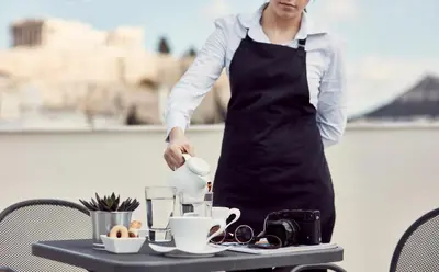 a woman in an apron standing next to a table at Acropolis Hill Hotel in Athens